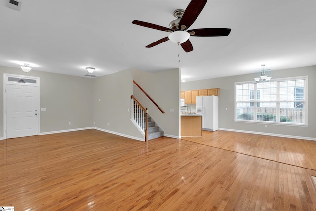 unfurnished living room with ceiling fan with notable chandelier and light hardwood / wood-style floors