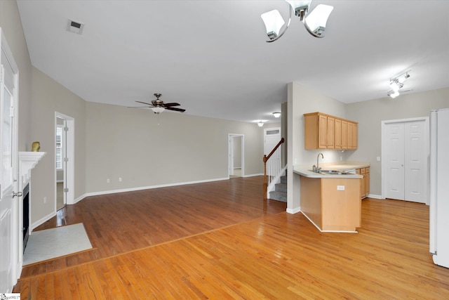 kitchen with kitchen peninsula, ceiling fan, light brown cabinetry, light wood-type flooring, and sink