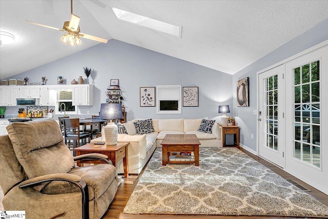 living room with ceiling fan, a textured ceiling, hardwood / wood-style flooring, lofted ceiling with skylight, and sink