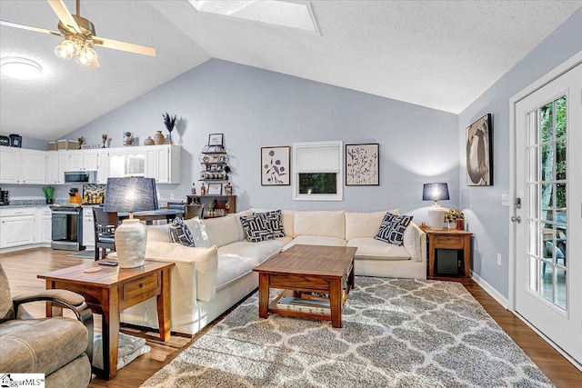 living room featuring lofted ceiling with skylight, a textured ceiling, hardwood / wood-style floors, and ceiling fan