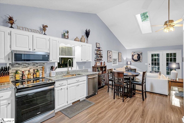 kitchen featuring vaulted ceiling with skylight, appliances with stainless steel finishes, sink, and white cabinets