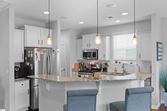 kitchen featuring a breakfast bar area, hanging light fixtures, sink, white cabinets, and appliances with stainless steel finishes