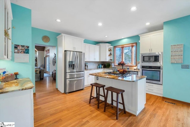 kitchen with white cabinets, a kitchen island, appliances with stainless steel finishes, and light hardwood / wood-style flooring