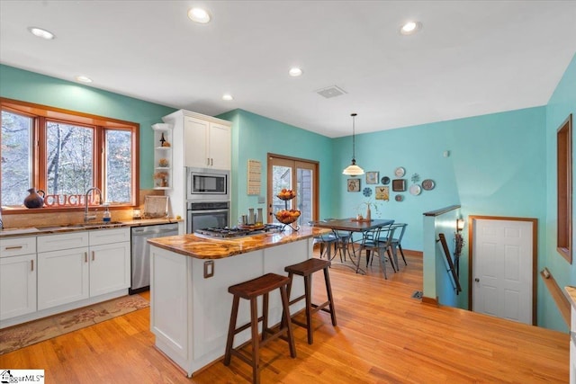 kitchen with white cabinets, light hardwood / wood-style flooring, appliances with stainless steel finishes, and decorative light fixtures