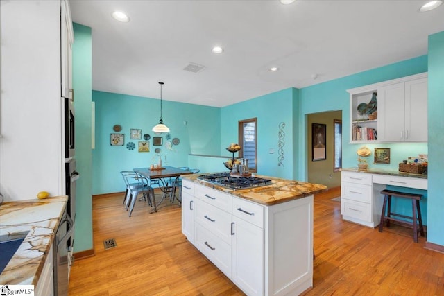 kitchen featuring stainless steel gas stovetop, a center island, white cabinets, light wood-type flooring, and decorative light fixtures