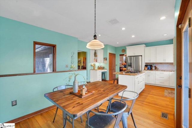 kitchen with a kitchen island, white cabinetry, light wood-type flooring, stainless steel fridge with ice dispenser, and pendant lighting