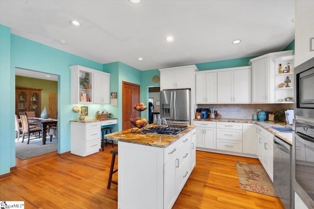 kitchen with stainless steel appliances, light hardwood / wood-style floors, white cabinets, a breakfast bar area, and a kitchen island