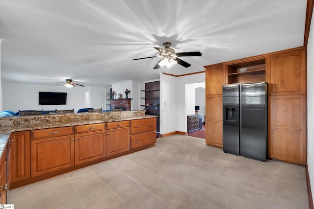 kitchen featuring a brick fireplace, stainless steel refrigerator with ice dispenser, ceiling fan, and light stone countertops