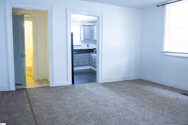 unfurnished room featuring a wealth of natural light, a textured ceiling, and dark colored carpet