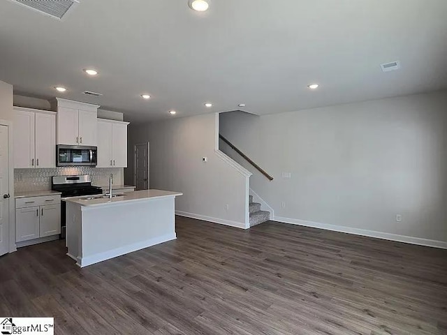 kitchen featuring dark wood-type flooring, white cabinets, decorative backsplash, a kitchen island with sink, and appliances with stainless steel finishes