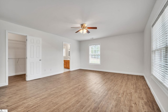 unfurnished bedroom with ensuite bathroom, ceiling fan, light wood-type flooring, and a spacious closet