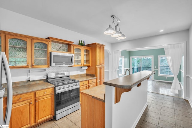 kitchen featuring stainless steel appliances, light wood-type flooring, a kitchen island, pendant lighting, and decorative backsplash