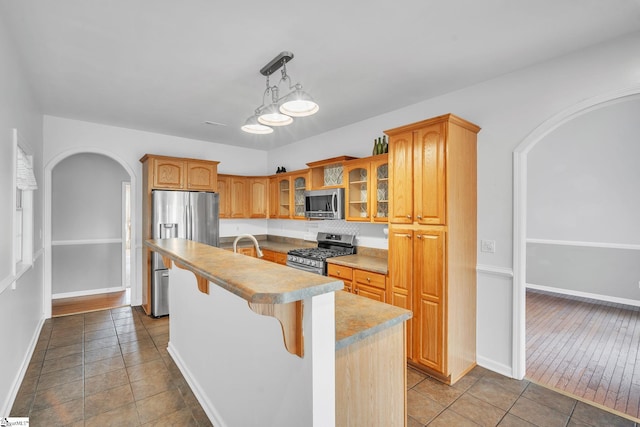 kitchen featuring light wood-type flooring, appliances with stainless steel finishes, pendant lighting, a breakfast bar, and a kitchen island with sink