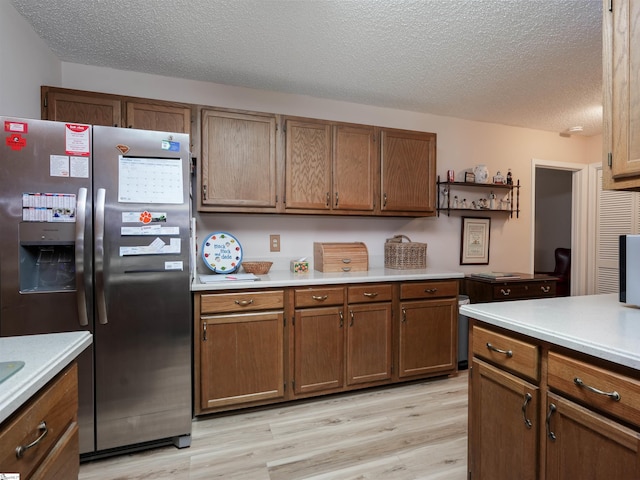 kitchen featuring light wood-type flooring, stainless steel fridge with ice dispenser, and a textured ceiling