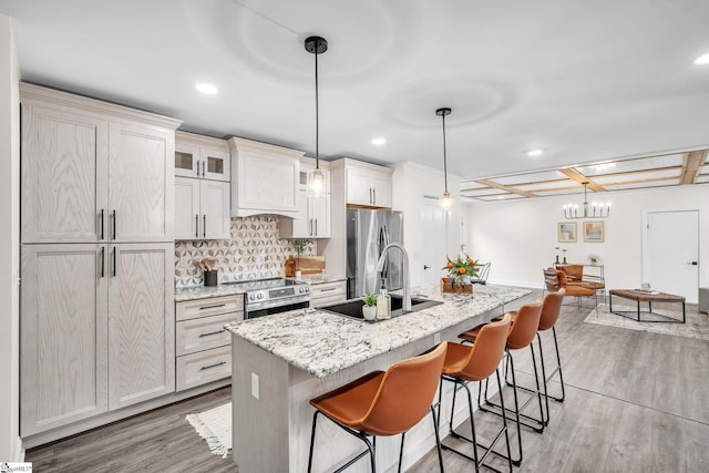 kitchen featuring appliances with stainless steel finishes, pendant lighting, sink, light stone counters, and a center island with sink