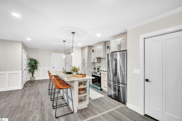 kitchen with pendant lighting, stainless steel appliances, a kitchen island with sink, and light hardwood / wood-style flooring