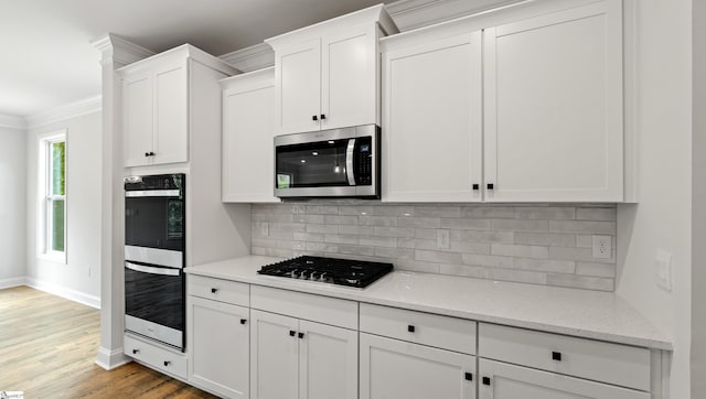kitchen featuring stainless steel appliances, crown molding, white cabinets, baseboards, and decorative backsplash