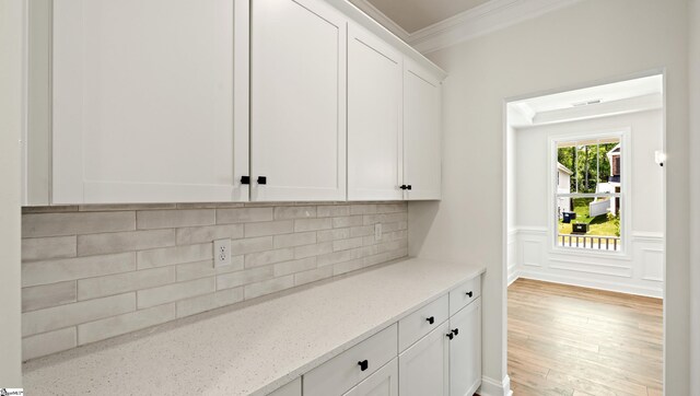 kitchen featuring crown molding, white cabinets, decorative backsplash, light stone countertops, and light wood-style flooring