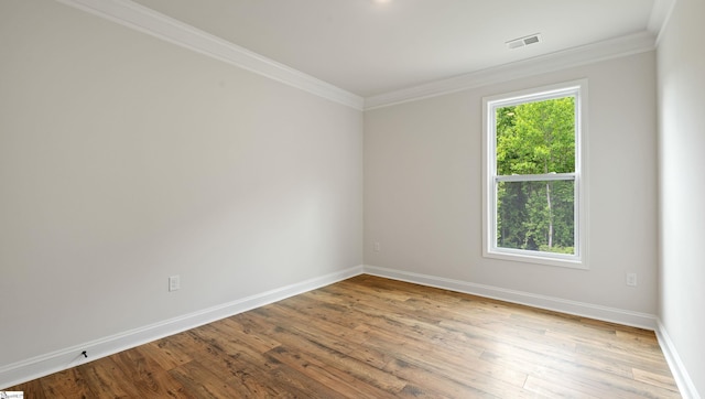 spare room featuring wood finished floors, crown molding, and baseboards