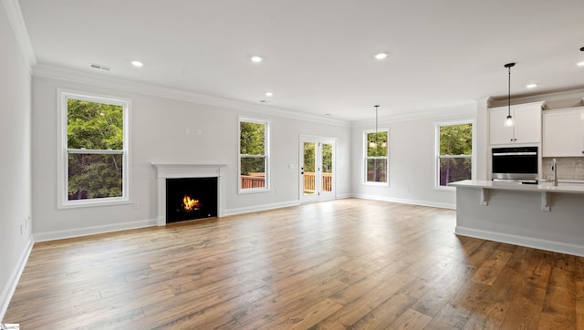 unfurnished living room with healthy amount of natural light, a warm lit fireplace, light wood-style floors, crown molding, and recessed lighting