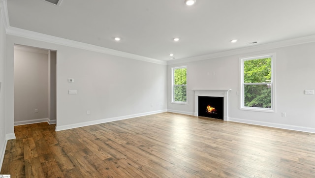 unfurnished living room featuring wood finished floors, ornamental molding, recessed lighting, a warm lit fireplace, and baseboards