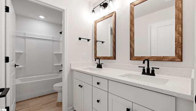 bathroom featuring toilet, double vanity, wood finished floors, and  shower combination
