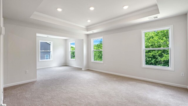 empty room with a tray ceiling, crown molding, carpet, baseboards, and recessed lighting