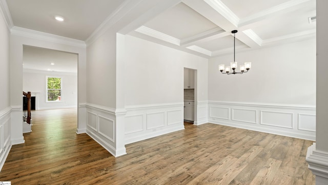 unfurnished dining area with wood finished floors, a chandelier, beamed ceiling, a wainscoted wall, and coffered ceiling