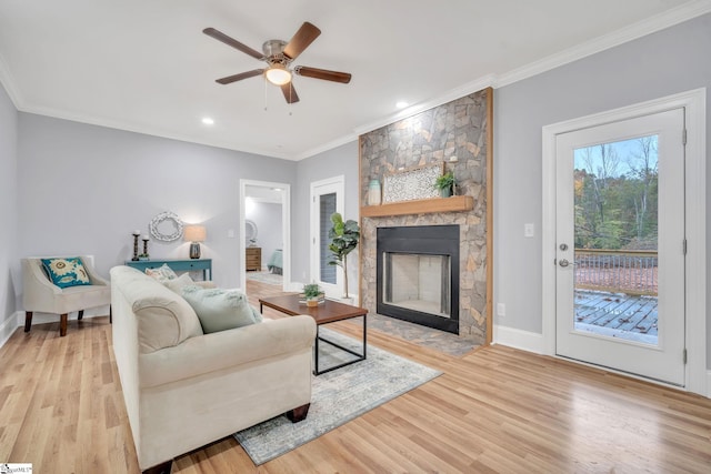 living room with a fireplace, light hardwood / wood-style flooring, ceiling fan, and crown molding