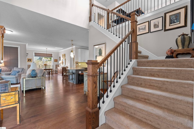 staircase featuring a towering ceiling, wood-type flooring, crown molding, and a notable chandelier