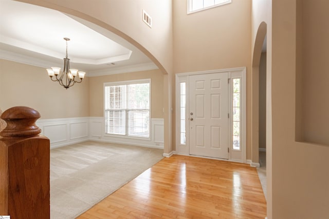 foyer featuring a tray ceiling, an inviting chandelier, crown molding, and light hardwood / wood-style flooring