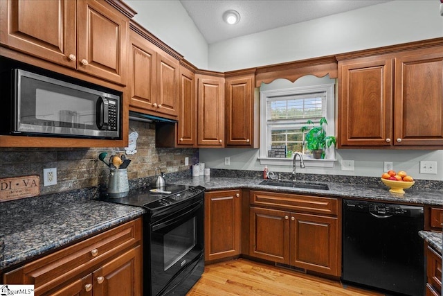 kitchen with lofted ceiling, black appliances, sink, light hardwood / wood-style flooring, and dark stone countertops