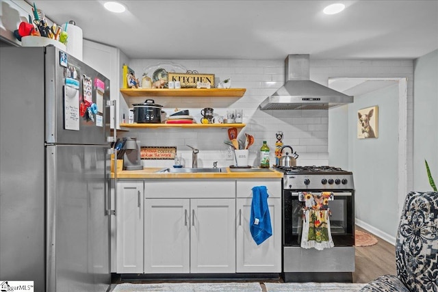 kitchen featuring dark hardwood / wood-style flooring, white cabinets, sink, wall chimney range hood, and appliances with stainless steel finishes