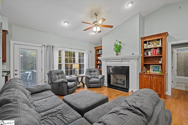 living room with light hardwood / wood-style floors, lofted ceiling, ceiling fan, and a tile fireplace