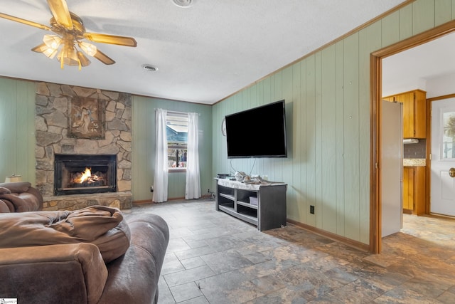 living room featuring crown molding, a fireplace, a textured ceiling, wooden walls, and ceiling fan