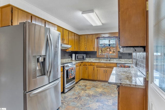 kitchen featuring light stone counters, a textured ceiling, sink, tasteful backsplash, and appliances with stainless steel finishes