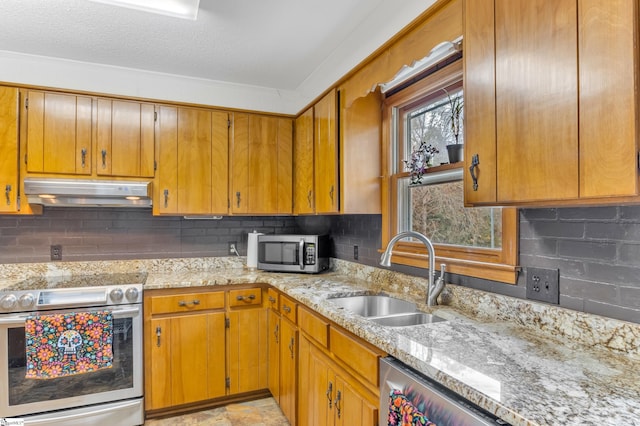 kitchen featuring stainless steel appliances, sink, light stone counters, a textured ceiling, and backsplash