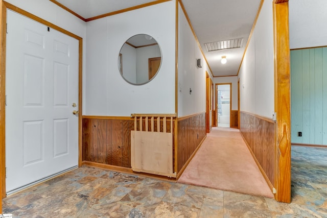 carpeted foyer featuring wooden walls and crown molding