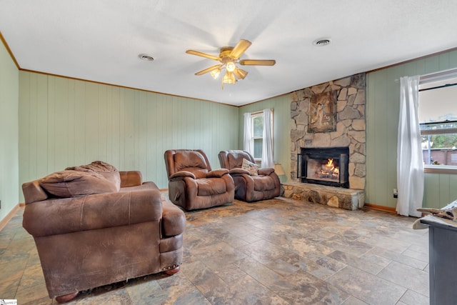 living room featuring a stone fireplace, wood walls, and ceiling fan