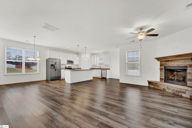 unfurnished living room with dark hardwood / wood-style floors, a stone fireplace, and ceiling fan with notable chandelier