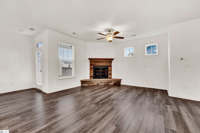 unfurnished living room with dark hardwood / wood-style flooring, a stone fireplace, and ceiling fan