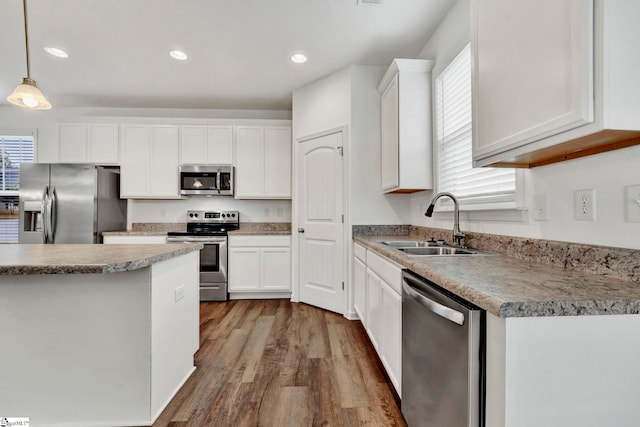 kitchen featuring stainless steel appliances, hanging light fixtures, hardwood / wood-style flooring, sink, and white cabinetry