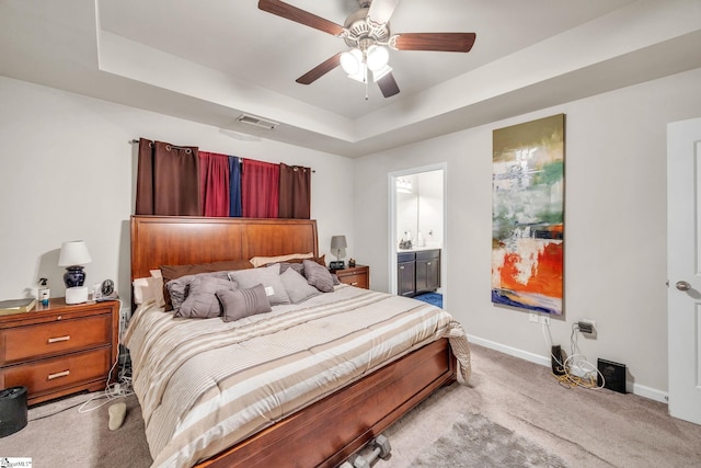 bedroom featuring ensuite bathroom, light carpet, ceiling fan, and a raised ceiling