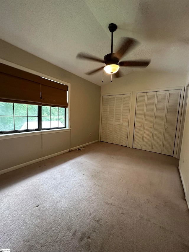 unfurnished bedroom featuring multiple closets, light carpet, a textured ceiling, and ceiling fan