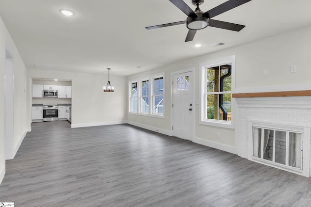 unfurnished living room featuring hardwood / wood-style floors, ceiling fan with notable chandelier, and a fireplace