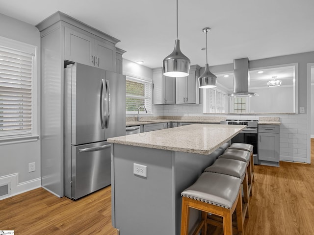 kitchen with stainless steel appliances, island exhaust hood, a kitchen island, and light hardwood / wood-style floors