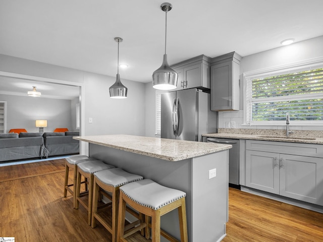 kitchen with appliances with stainless steel finishes, sink, light hardwood / wood-style floors, and hanging light fixtures