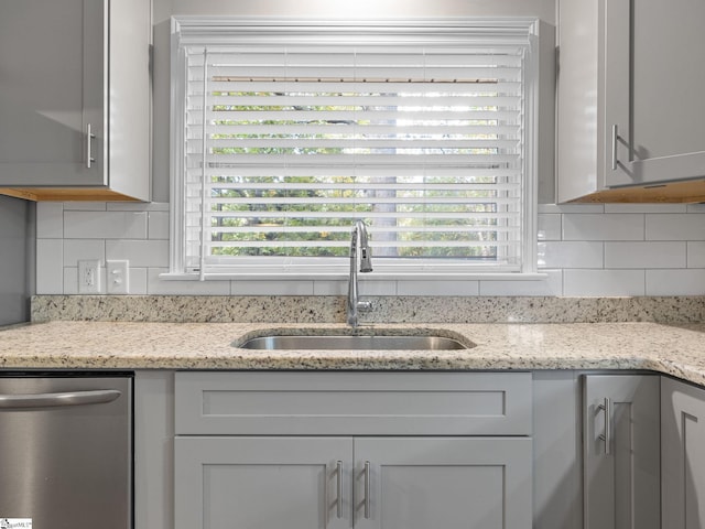 interior details with gray cabinets, stainless steel dishwasher, sink, and light stone countertops