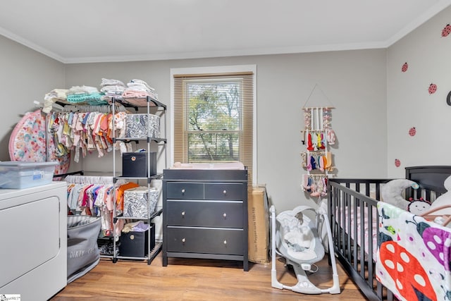 bedroom with a crib, light hardwood / wood-style flooring, washer / clothes dryer, and ornamental molding