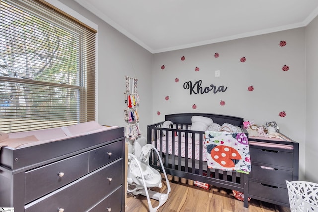 bedroom with ornamental molding, light wood-type flooring, and a nursery area